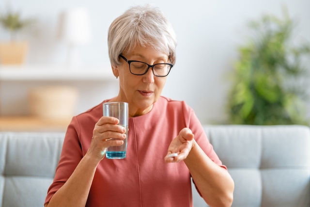 Mujer con una tableta de oxibutinina en la mano y un vaso de agua