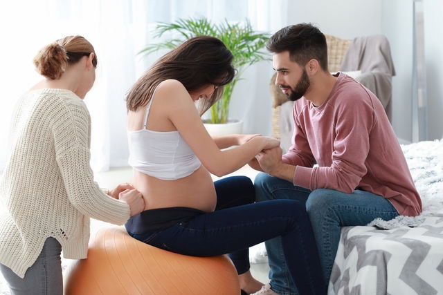 Woman in labor, with male partner and female aiding through contraction