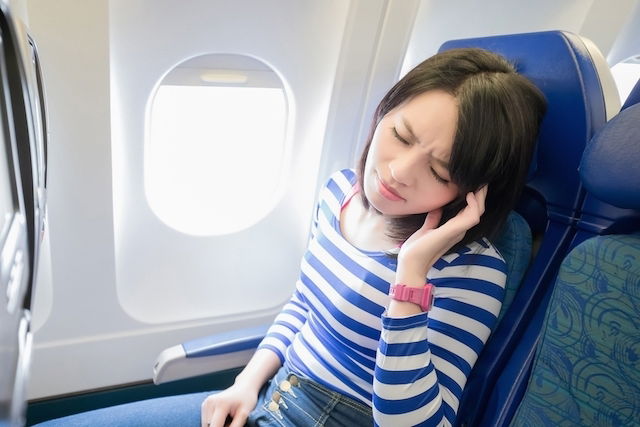 woman on plane holding her hand against her ear in pain