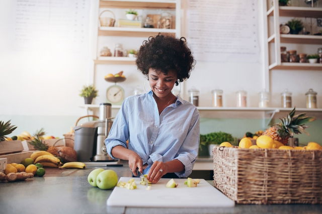 Mulher cortando frutas na bancada de uma cozinha