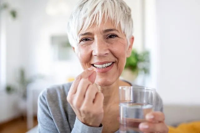 Mujer mayor tomando una pastilla de fenofibrato