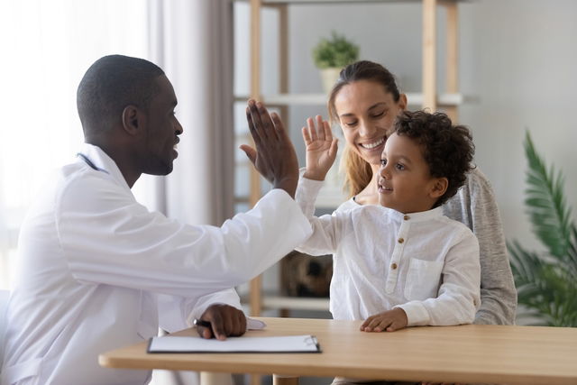 Médico cumprimentando uma criança no colo da mãe ao iniciar a consulta