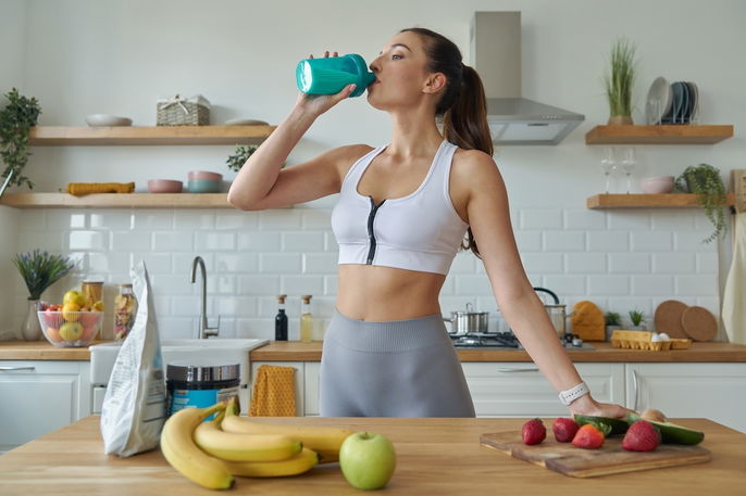 woman in kitchen in workout clothes drinking out of a bottle