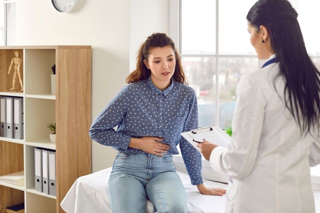 Mujer consultando a médico indicando con la mano el dolor que tiene en la barriga