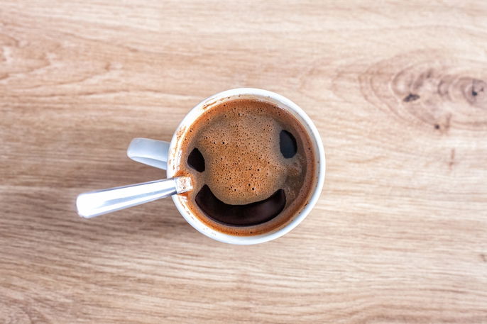 Uma xícara cheia de café com a espuma na sua superfície formando um rosto sorrindo