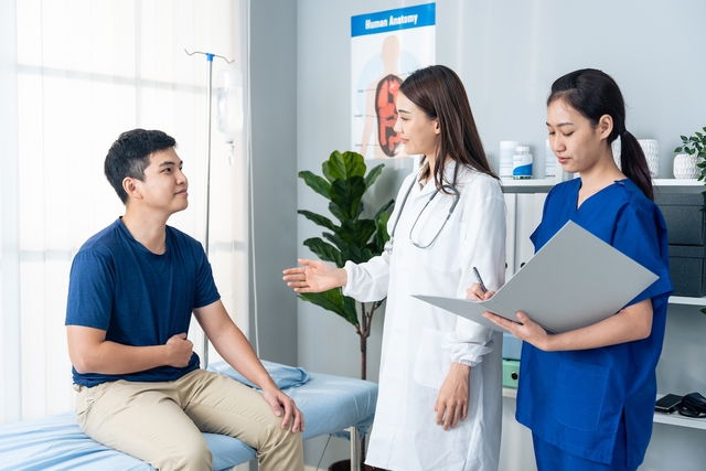 Homen jovem com uma das mãos no abdome enquanto conversa com a médica no consultório sobre o diagnós