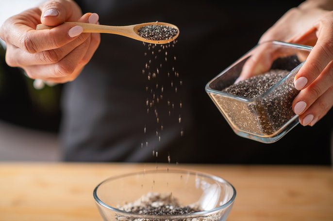 person's hand sprinkling a spoonful of chia seeds
