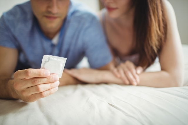 Heterosexual couple looking at condom package on bed