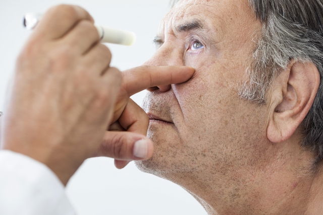 Hombre mirando hacia arriba mientras el médico examina su ojo con una fuente de luz