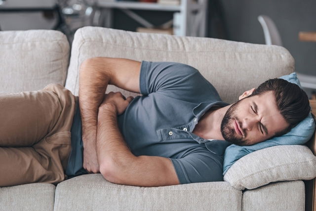 Man lying on couch and clutching abdomen in pain