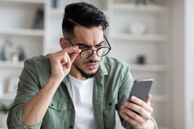 Hombre sosteniendo los lentes para intentar leer el teléfono