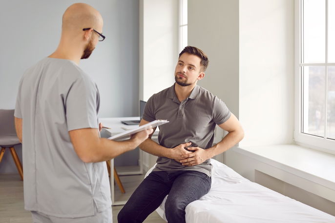 Joven explicando al médico el malestar que siente en el abdomen