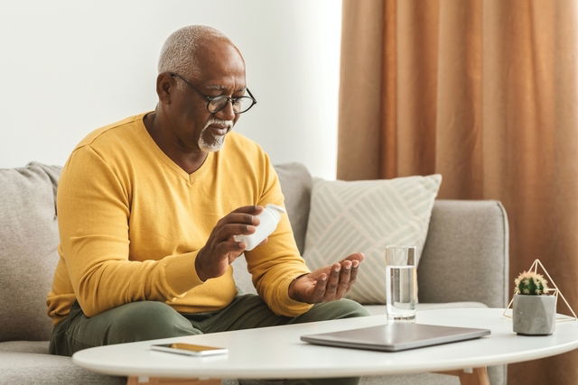 Man sitting on couch taking medication with glass of water