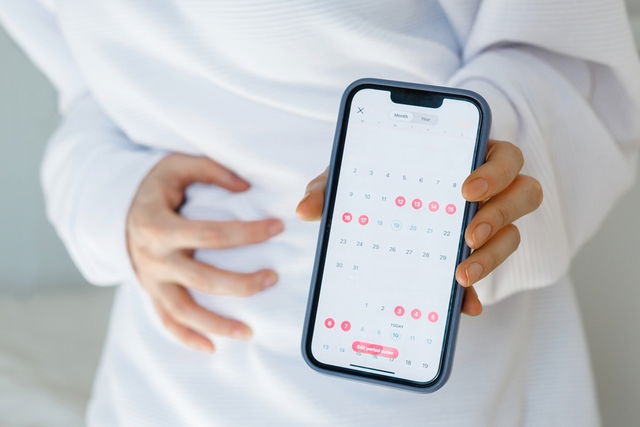 Woman holding phone with menstrual calendar