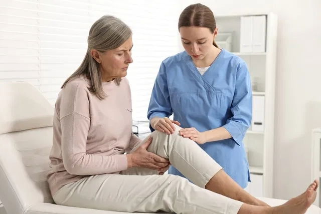 Traumatóloga revisando la rodilla de una mujer mayor