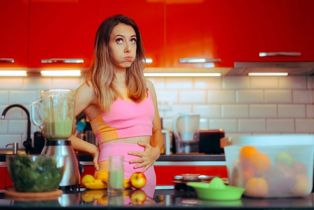 Girl in kitchen with abdominal pain, thinking about what to eat