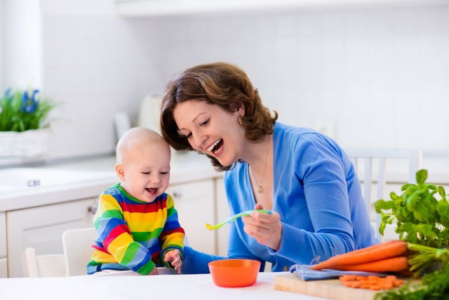 Mulher dando papa de cenoura para o bebê