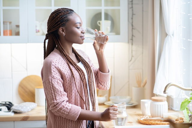 Mulher tomando um copo de água na cozinha