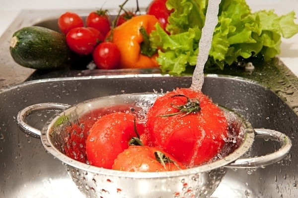 tomatoes being washed in a colander with running water