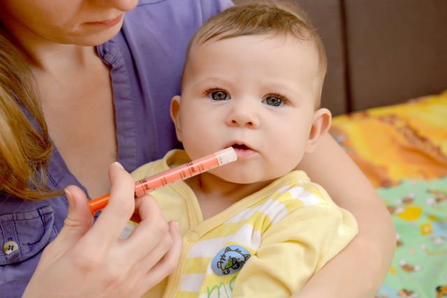 Mãe dando remédio na boca do bebê