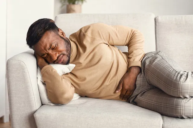 homme couché sur le canapé se tenant le ventre souffrant de nausées