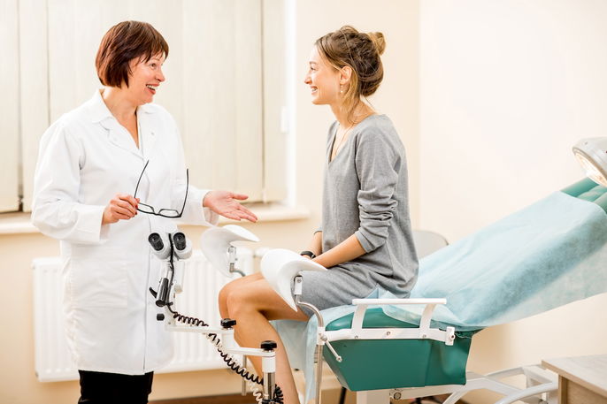 woman in patient gown talking to gynecologist