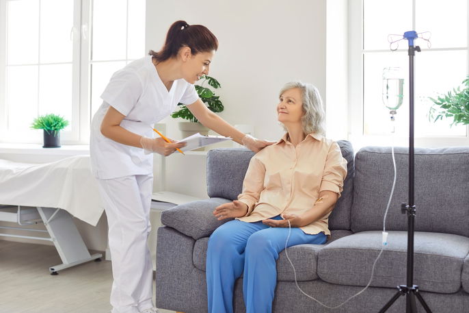 female healthcare provider checking on an older female patient receiving an IV infusion