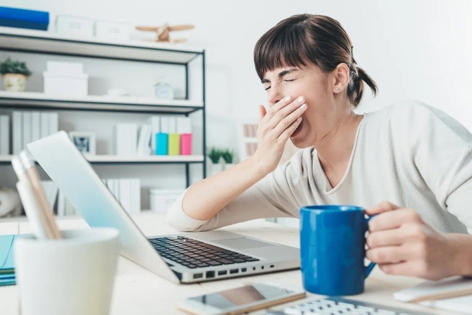 woman at her desk holding a cup of coffee and yawning