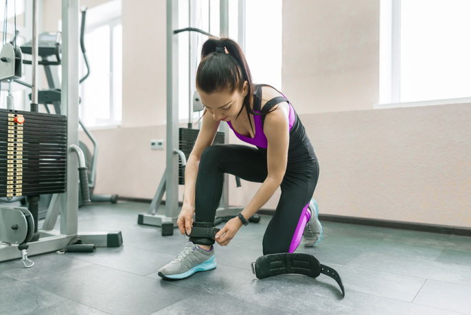 woman putting ankle strap on to use the cable machine at the gym