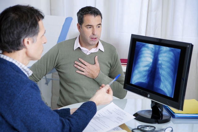 patient en consultation médicale se touchant le thorax et observant une radiographie pulmonaire