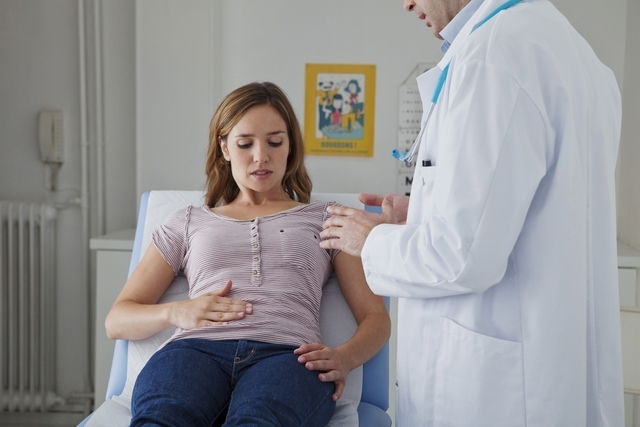 Woman palpating abdomen as doctor assesses