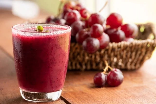 Vaso de jugo cerca de una canasta con cajas de uvas